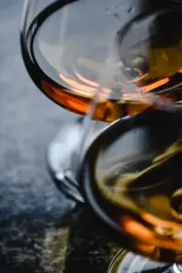 兩只酒杯與琥珀色酒液的近拍,呈現玻璃反光與暖色光影