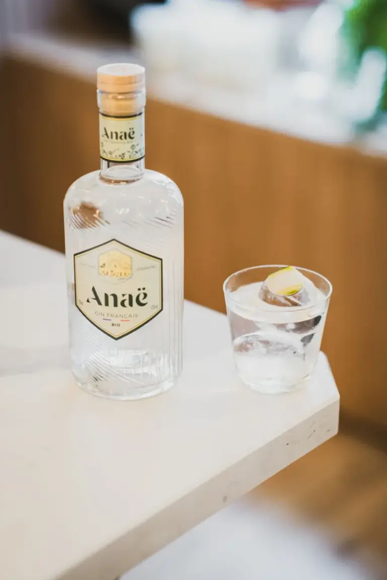 白色桌面上的琴酒瓶與加冰、柑橘裝飾的酒杯