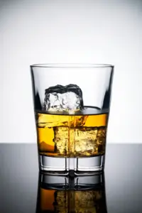 淺色背景前的威士忌矮杯、冰塊與桌面倒影