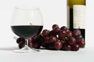 白色桌面上的紅酒杯、紫色葡萄與酒瓶