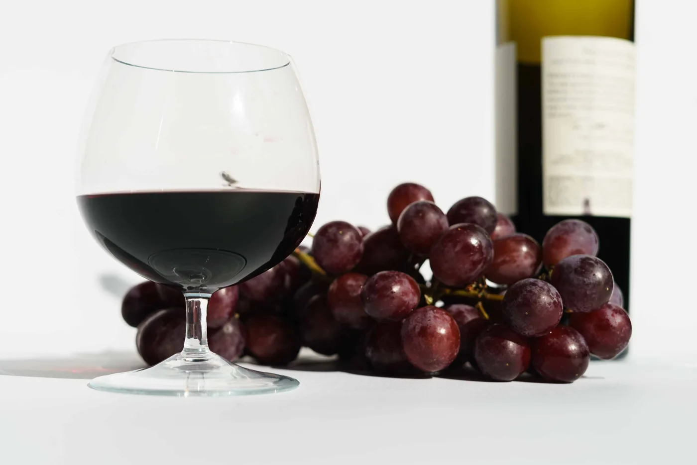 白色桌面上的紅酒杯、紫色葡萄與酒瓶